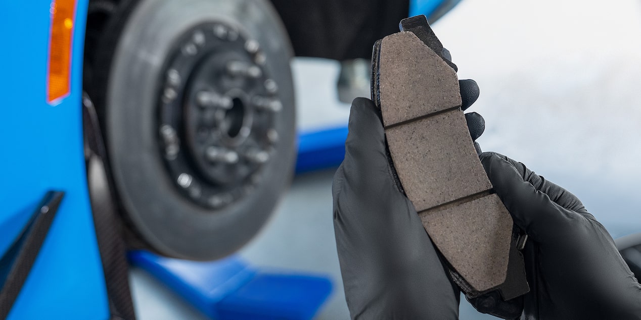 A View of a Mechanic Holding a Break Pad in Front of an Exposed Wheel