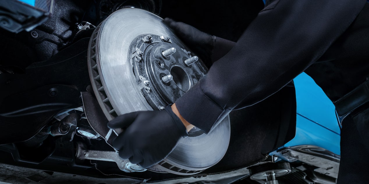A Mechanics Hands Are Seen Placing a Metal Break Rotor for a Vehicle