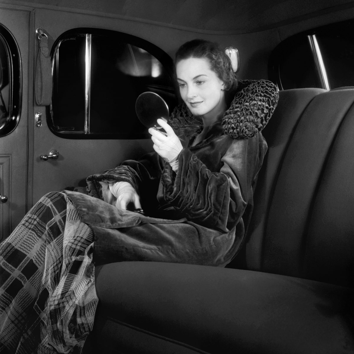 A Fashionably Dressed Woman Looking in a Make-up Mirror in the Second Row of a Classic Cadillac