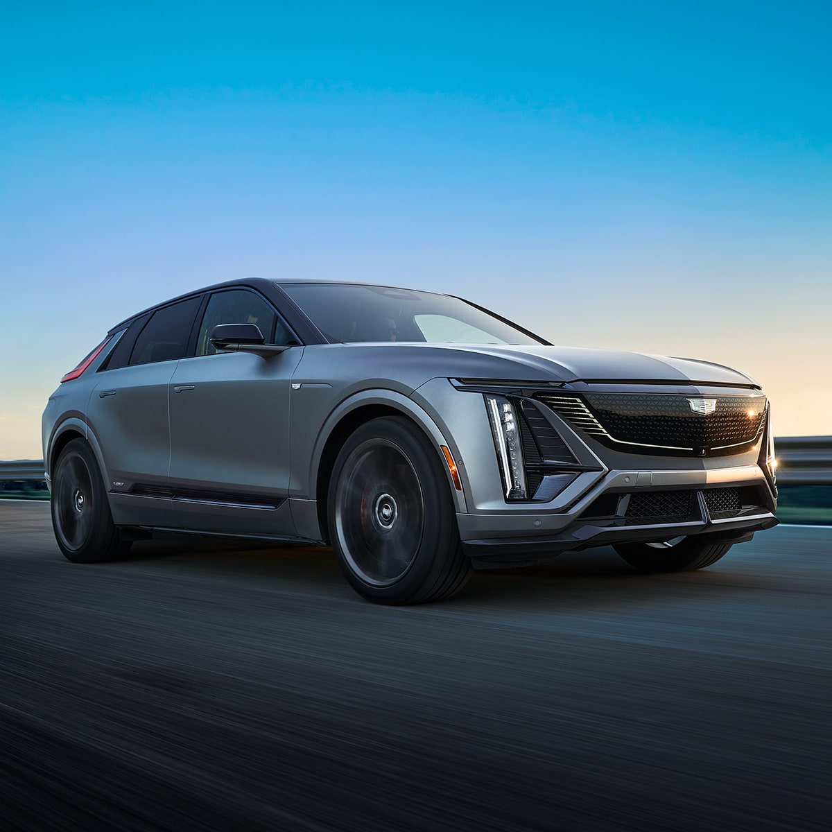 Low Passenger Three-quarters View of a Cadillac LYRIQ-V Driving Down a Road During a Sunset