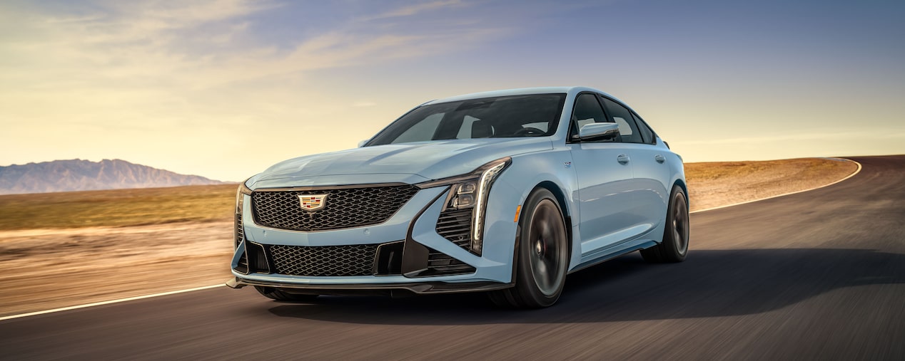 A Light Blue Cadillac V-Series Vehicle Driving Down a Road with Mountains in the Distance