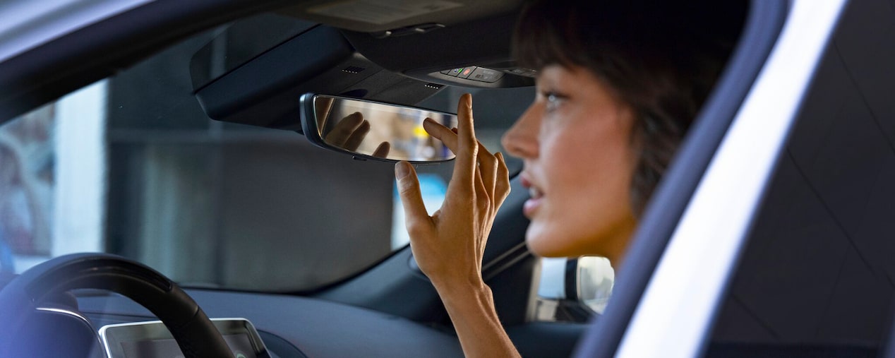 Primer plano de una mujer presionando el botón OnStar cerca del espejo retrovisor de un Cadillac