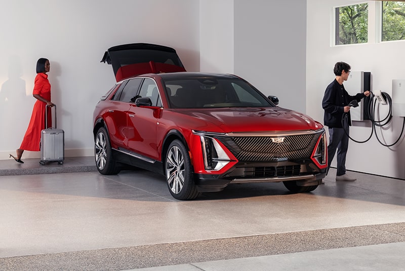 Un hombre carga un Cadillac EV rojo mientras una mujer coloca su equipaje en la cajuela