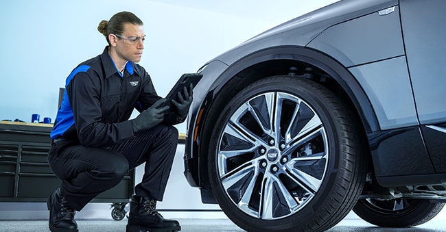 Cadillac Technician Kneeling Next to a Vehicle While Looking at a Tablet