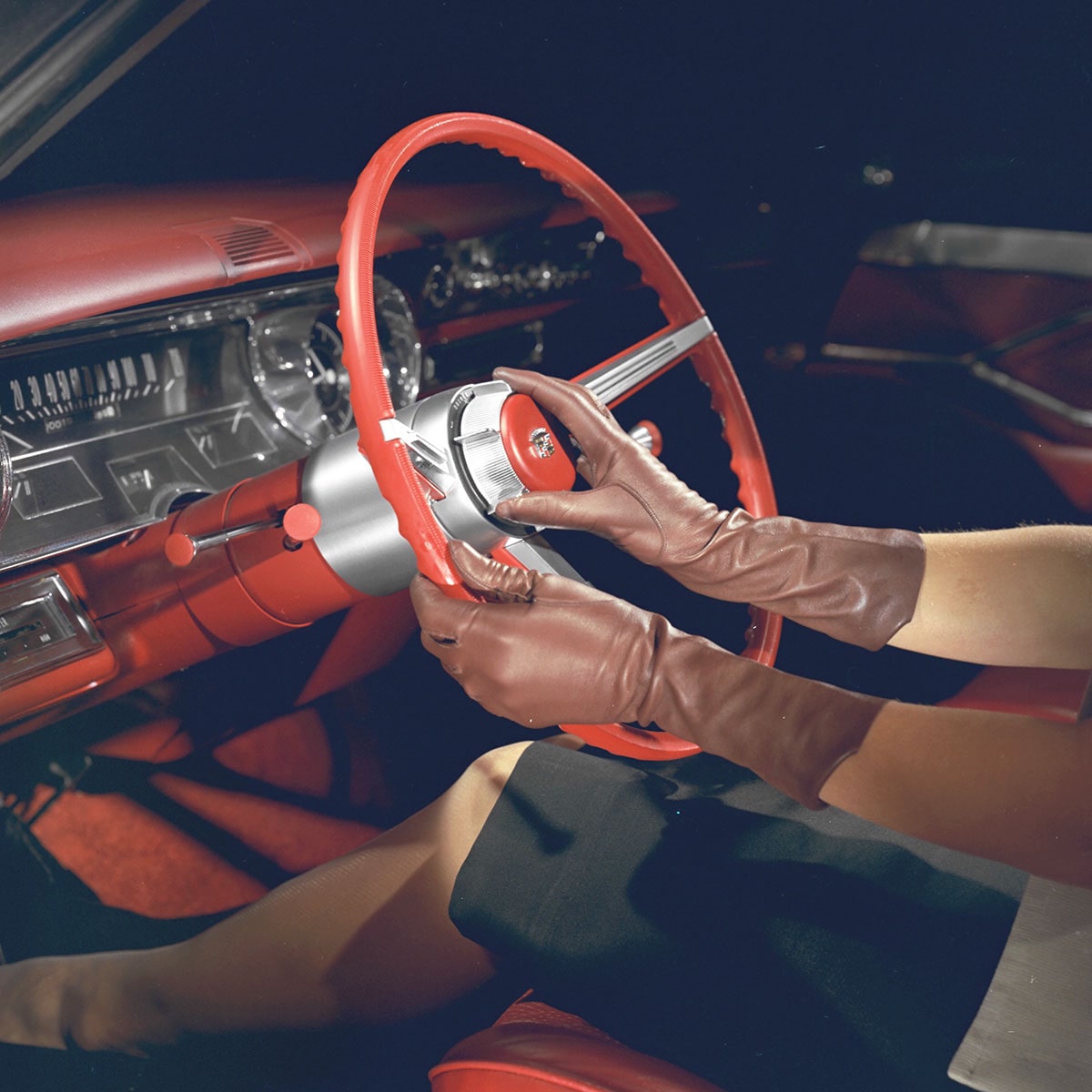 Una persona con guantes en el asiento del conductor de un Classic Cadillac, sujetando el volante