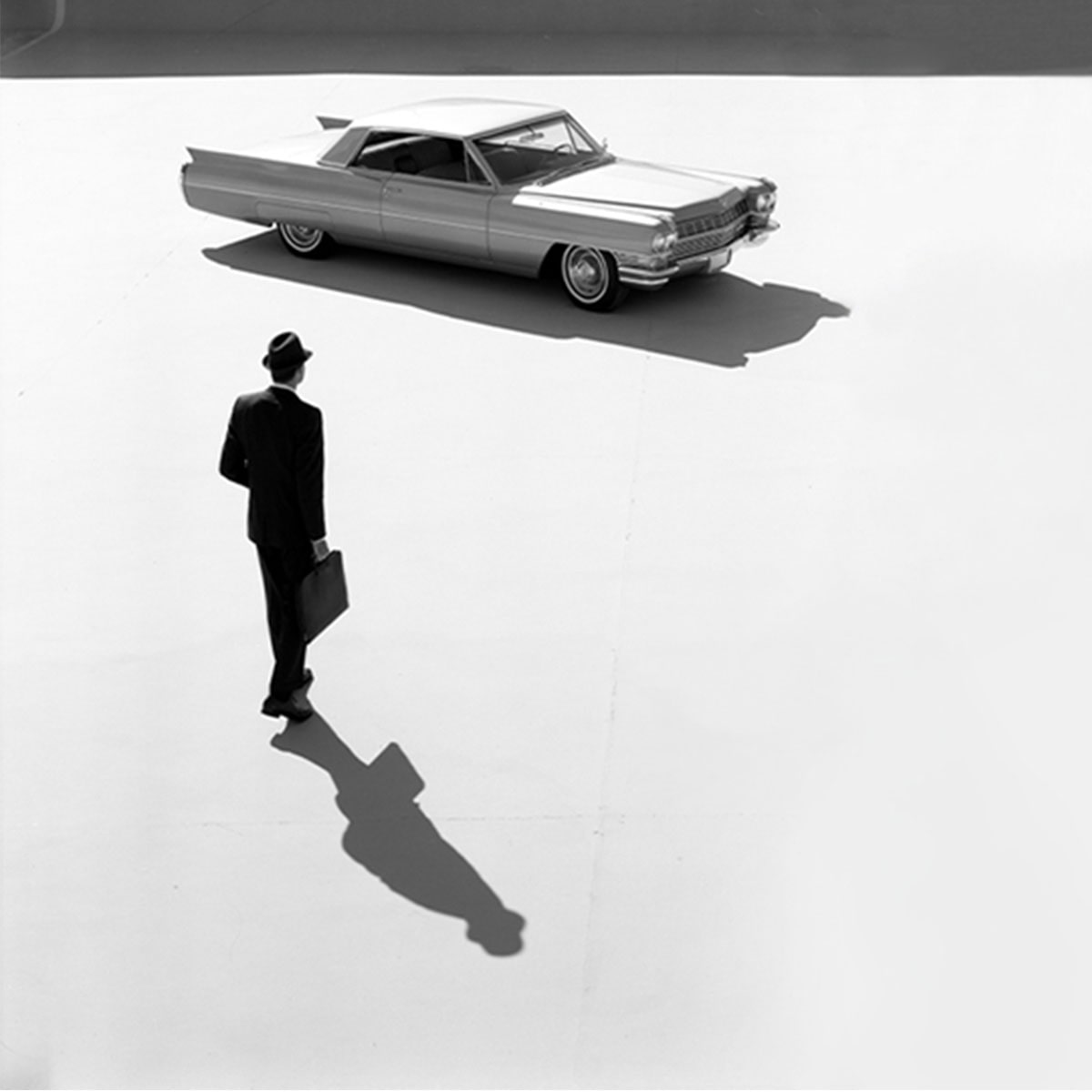 Vista general en blanco y negro de un empresario caminando hacia un Cadillac Series 62 Coupe 1964