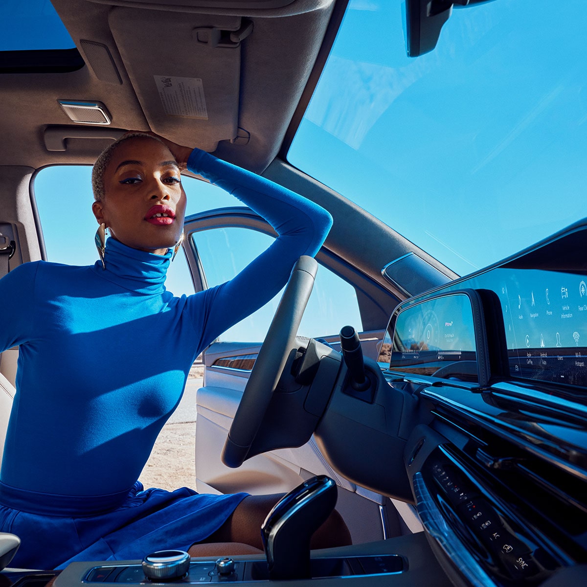 Una modelo posando en el asiento del conductor de un Cadillac, en un día soleado