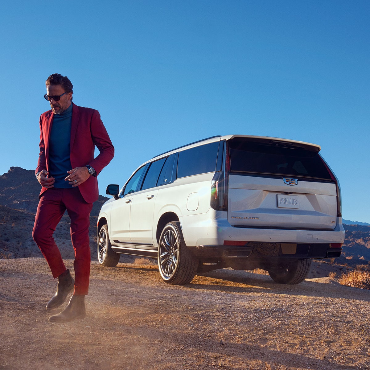 Una mujer vestida a la moda alejándose de una Cadillac Escalade Blanca en el desierto