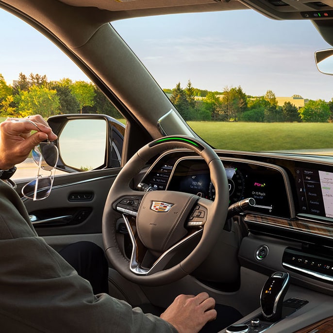 Un hombre sujetando unos anteojos de sol, sentado en el asiento del conductor de un vehículo Cadillac