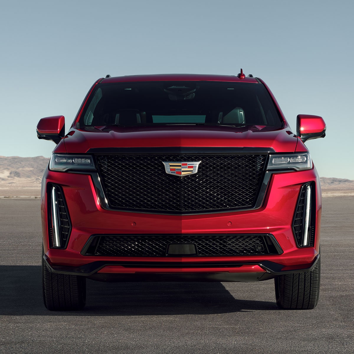 Vista delantera de una Cadillac Escalade Roja, estacionada junto a las montañas