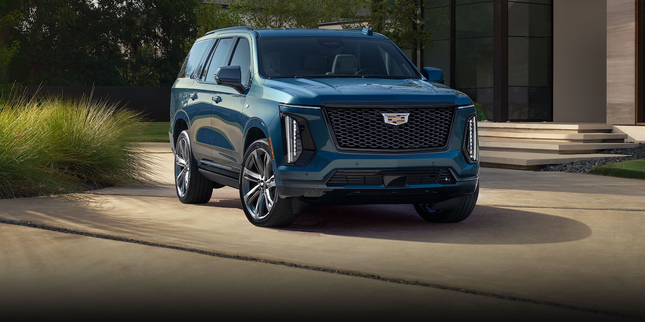 Three-quarter View of a Blue 2025 Cadillac Escalade Parked in Front of a Modern Home