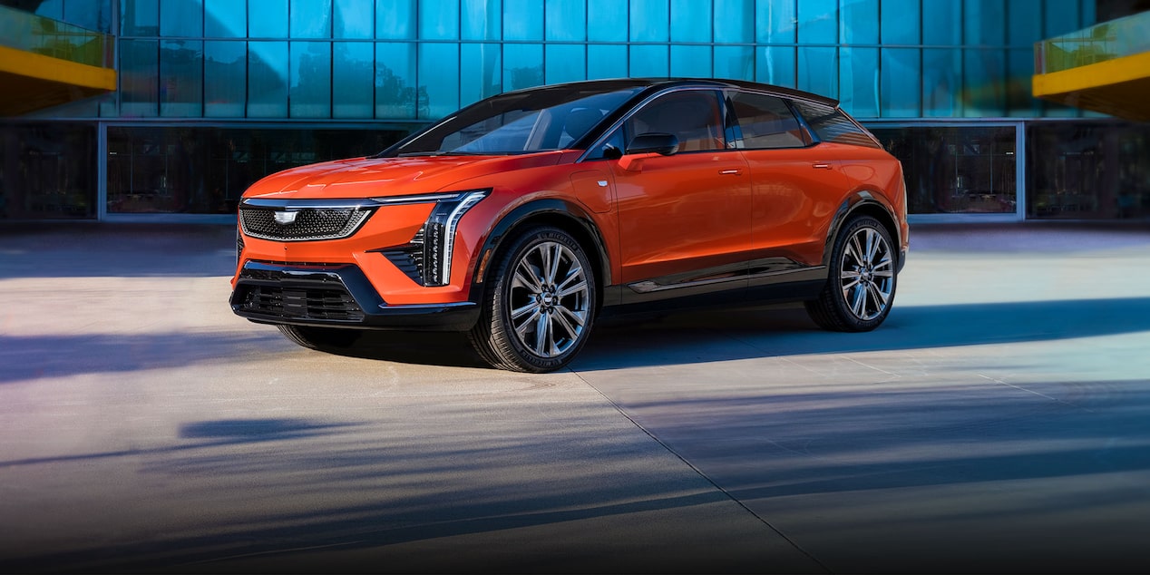 Vista de medio perfil de una Cadillac OPTIQ 2025 roja estacionada fuera de un edificio comercial