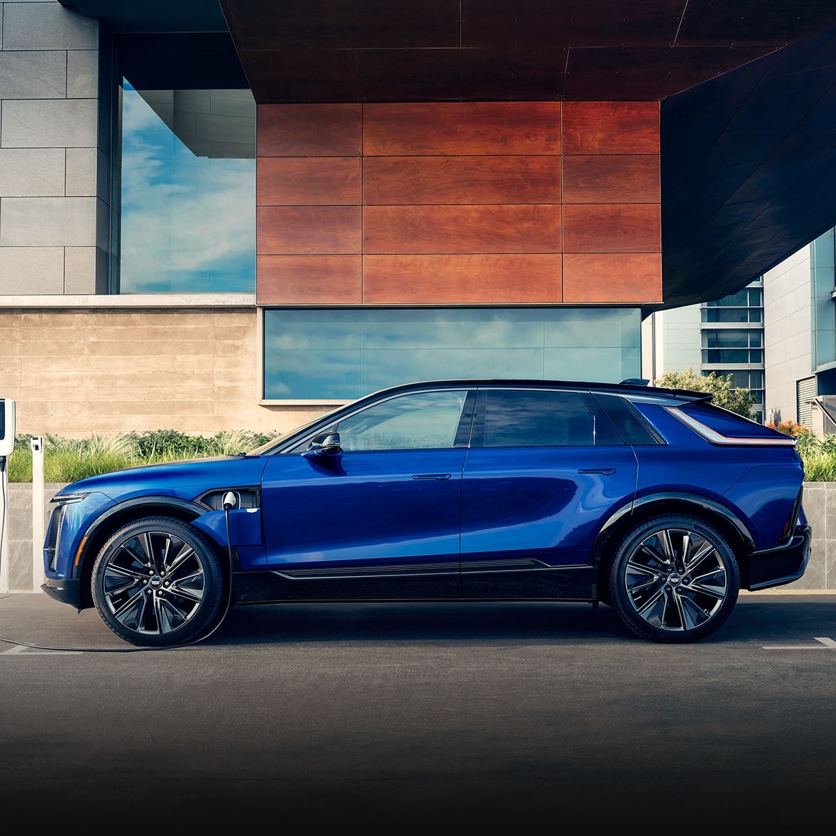 A Side Profile of a Blue 2024 Cadillac LYRIQ Charging Outside of a Building