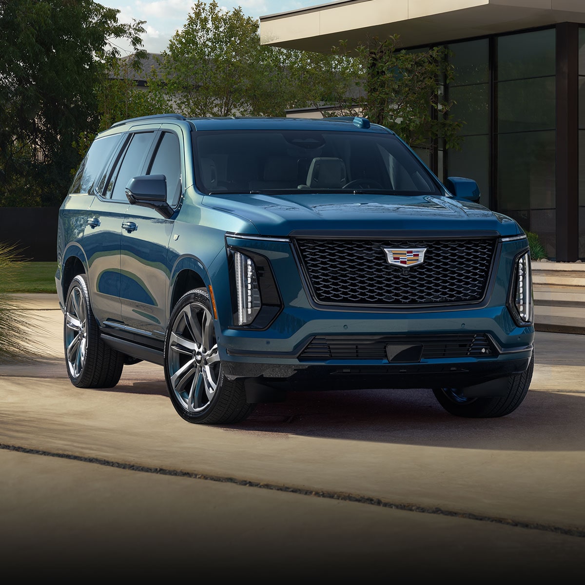 Three-quarter View of a Blue 2025 Cadillac Escalade Parked in Front of a Modern Home